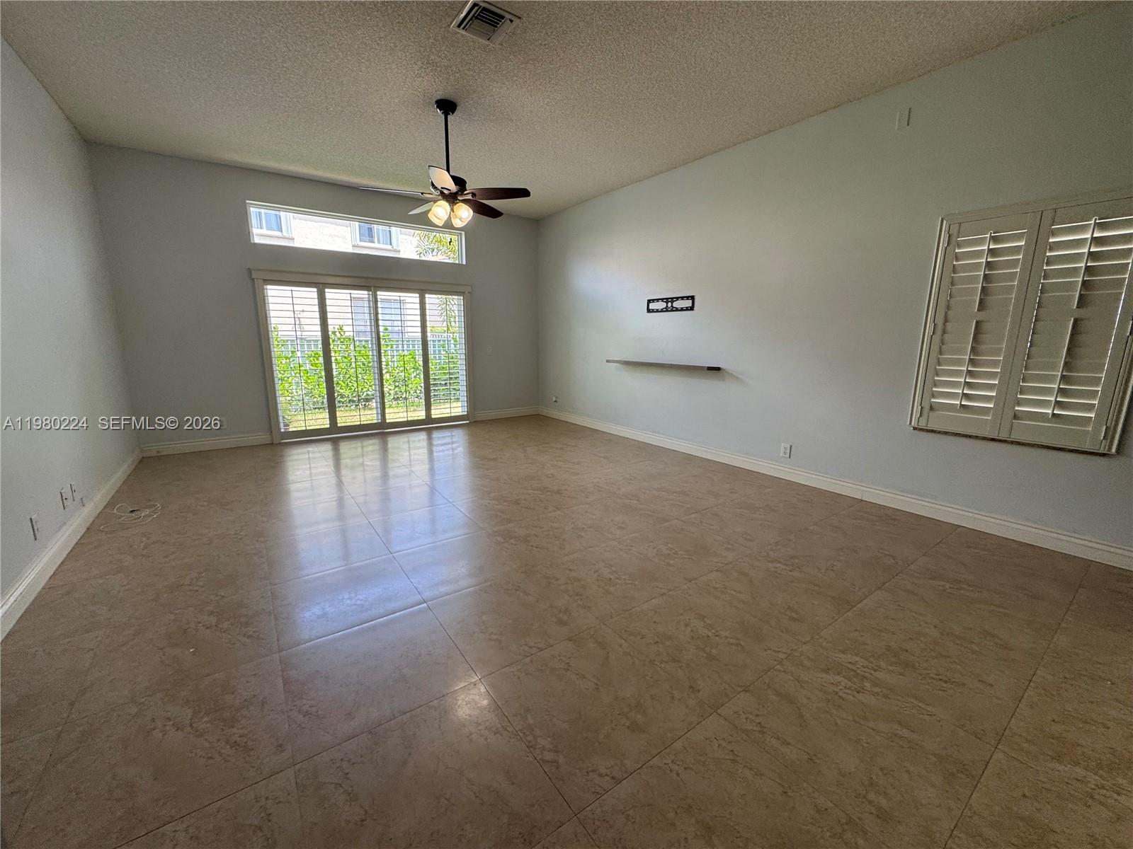 An empty living room features large beige floor tiles, a ceiling fan, and sliding doors — 4321 Willow Ridge Dr, Weston FL 33331, WESTON, FL