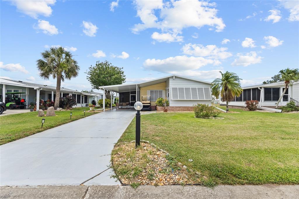 A single-story manufactured home features a concrete driveway, a carport, and a grassy front yard — 713 TANGERINE WOODS BOULEVARD, ENGLEWOOD, FL