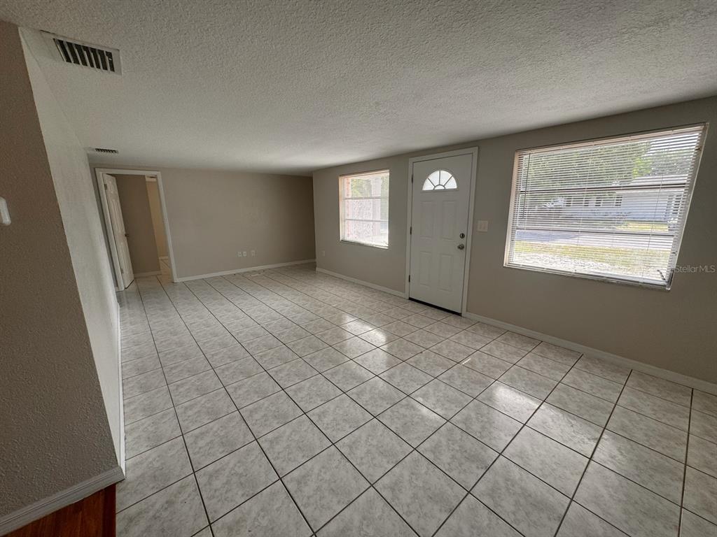 An empty living room features light-colored tile flooring, beige walls, and a white front door — 10731 PREMIER AVENUE, PORT RICHEY, FL
