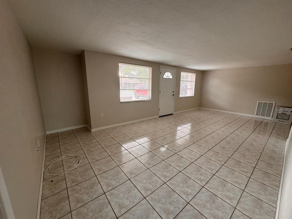An empty room with light-colored tile flooring, two windows, and a white entry door — 10731 PREMIER AVENUE, PORT RICHEY, FL