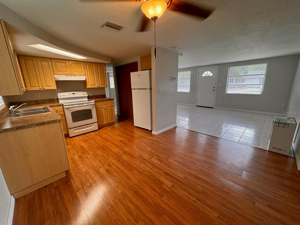 A kitchen with wood-look flooring and light wood cabinets opens into a tiled living area — 10731 PREMIER AVENUE, PORT RICHEY, FL