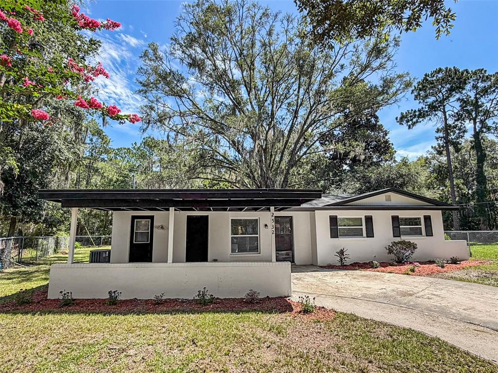 A single-story house with a flat-roofed front porch, a concrete driveway, and mature trees — 2532 NE 13TH AVENUE, GAINESVILLE, FL