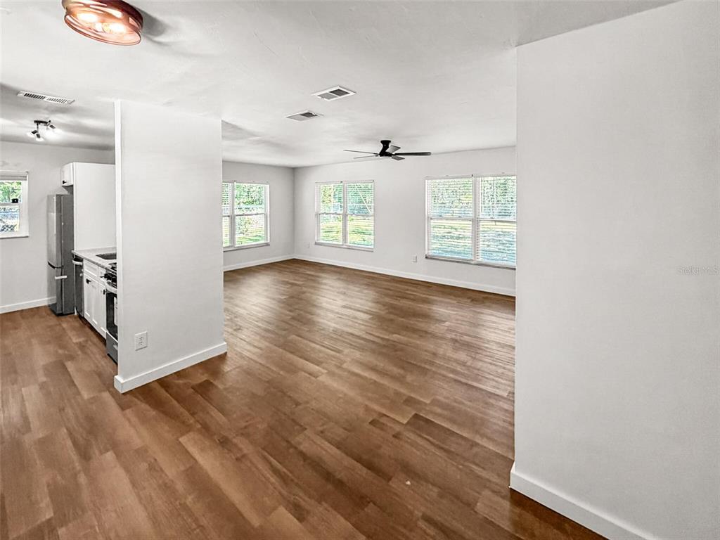 An open-concept living area features light wood-look flooring, white walls, and a partial kitchen wall — 2532 NE 13TH AVENUE, GAINESVILLE, FL