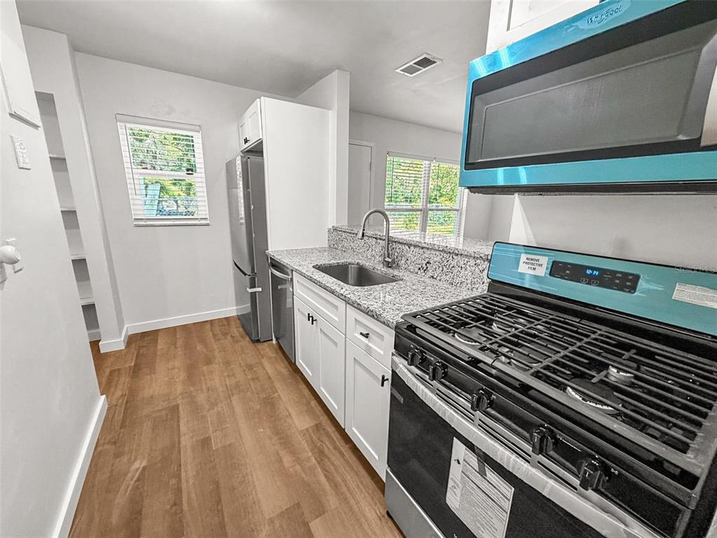 A kitchen features white cabinets, granite countertops, stainless steel appliances, and wood-look flooring — 2532 NE 13TH AVENUE, GAINESVILLE, FL
