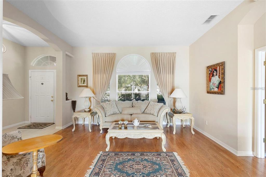 A living room with hardwood floors, a central sofa, arched window, and beige curtains — 713 MOUNTAIN ASH WAY, DELTONA, FL
