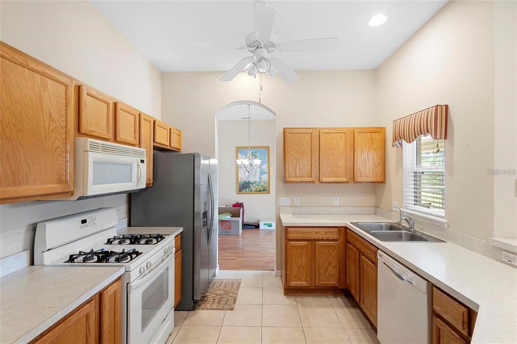 A kitchen with oak cabinets, white appliances, tile flooring, and a view into another room — 713 MOUNTAIN ASH WAY, DELTONA, FL