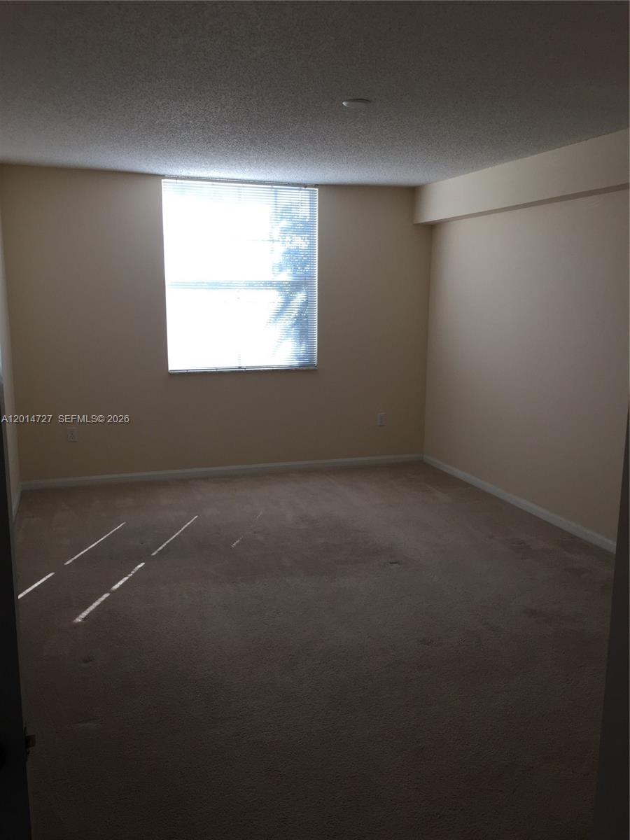 A kitchen with light wood cabinets and a stainless dishwasher overlooks a carpeted living area — 1900 Van Buren St # 214B, Hollywood FL 33020, HOLLYWOOD, FL
