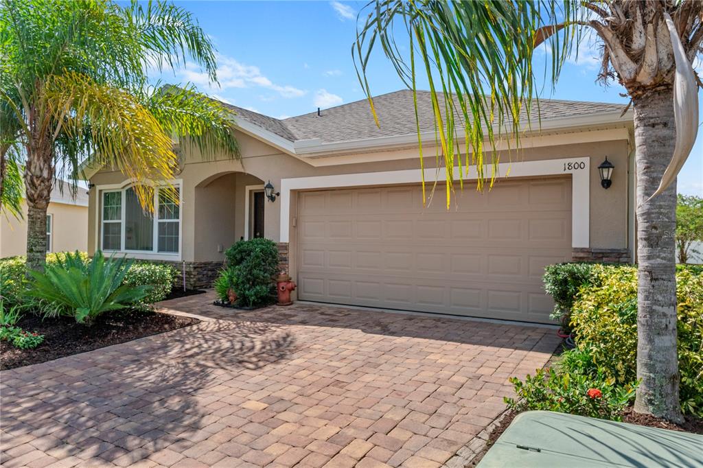 A single-story house with a beige stucco exterior, a two-car garage, and a paver driveway — 1800 STILLWOOD WAY, ST CLOUD, FL