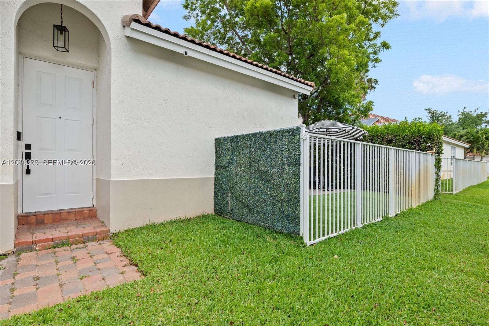 A white door with a brick walkway leads to a fenced yard with artificial greenery — 18755 SW 27th Ct, Miramar FL 33029, MIRAMAR, FL