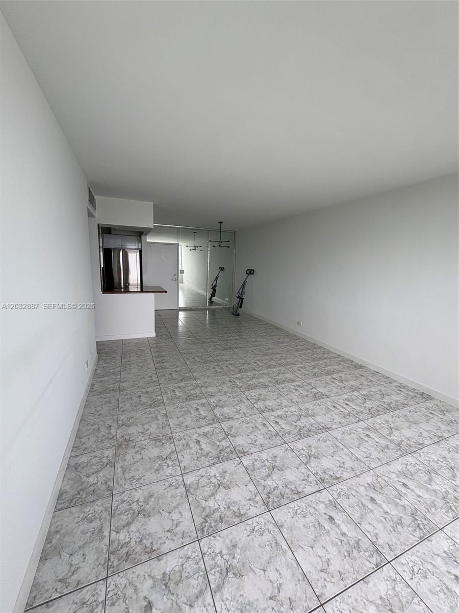 An empty room features white walls, gray tiled floors, a kitchen pass-through, and mirrored closet doors — 7441 Wayne Ave # 8B, Miami Beach FL 33141, MIAMI BEACH, FL