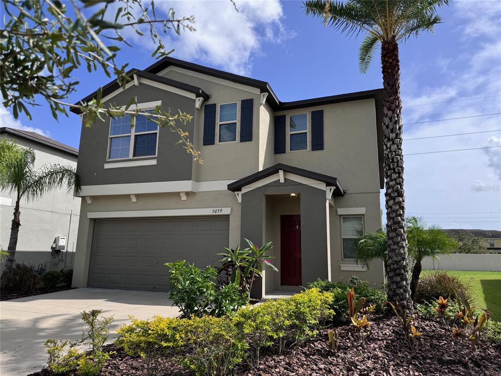 A two-story house with a two-car garage, dark shutters, and a red front door — 5059 WHITE CHICORY DRIVE, APOLLO BEACH, FL