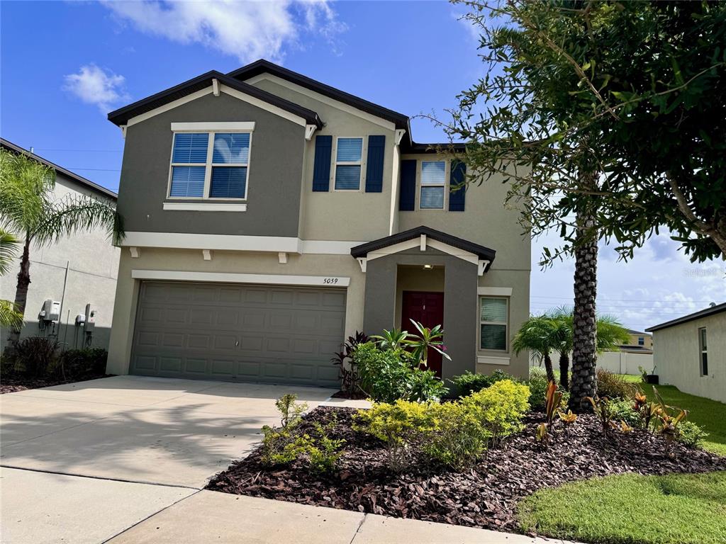A two-story suburban house features a two-car garage, a red front door, and landscaping — 5059 WHITE CHICORY DRIVE, APOLLO BEACH, FL