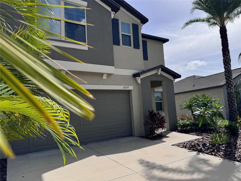 A two-story suburban house with a gray garage, beige stucco walls, and a palm tree — 5059 WHITE CHICORY DRIVE, APOLLO BEACH, FL
