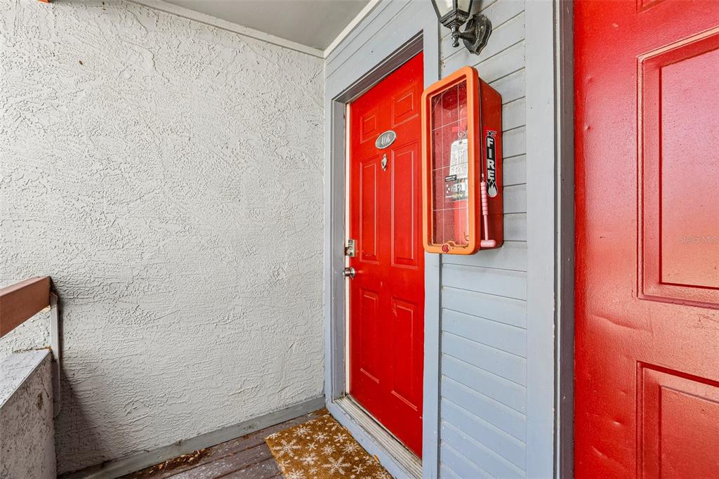 A red apartment door with a fire extinguisher cabinet mounted on the adjacent gray wall — 10263 GANDY BOULEVARD N UNIT 406, ST PETERSBURG, FL