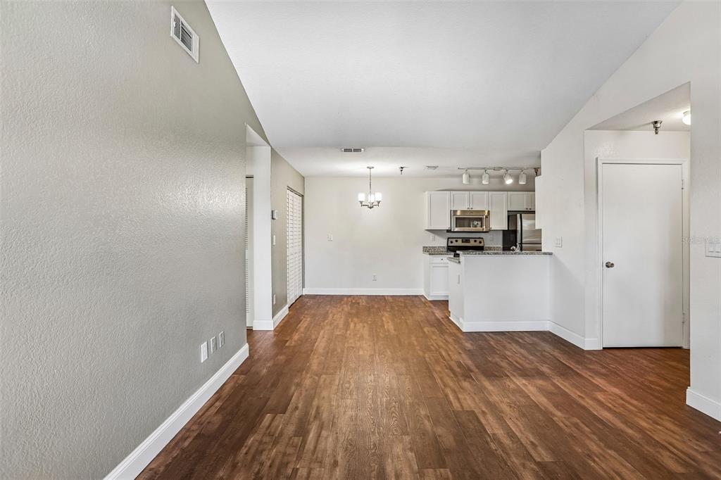 An open-concept dining area with wood-look flooring leads to a kitchen with white cabinetry — 10263 GANDY BOULEVARD N UNIT 406, ST PETERSBURG, FL