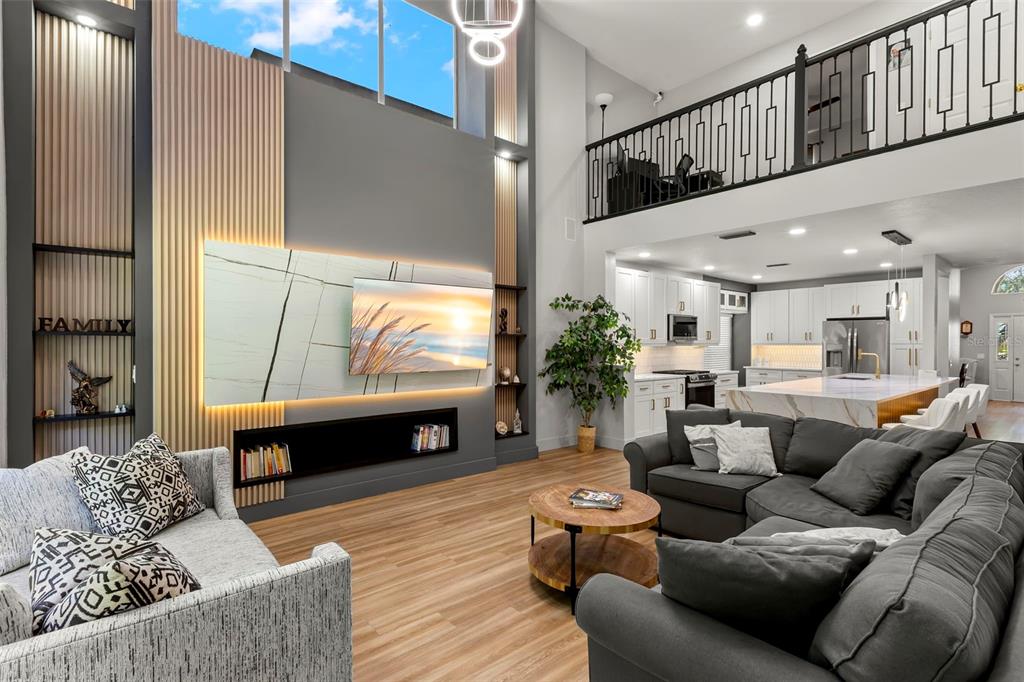 A modern open-concept living room features a large television, wood-slat accents, and a kitchen — 9915 HARTWELL BRIDGE CIRCLE, TAMPA, FL