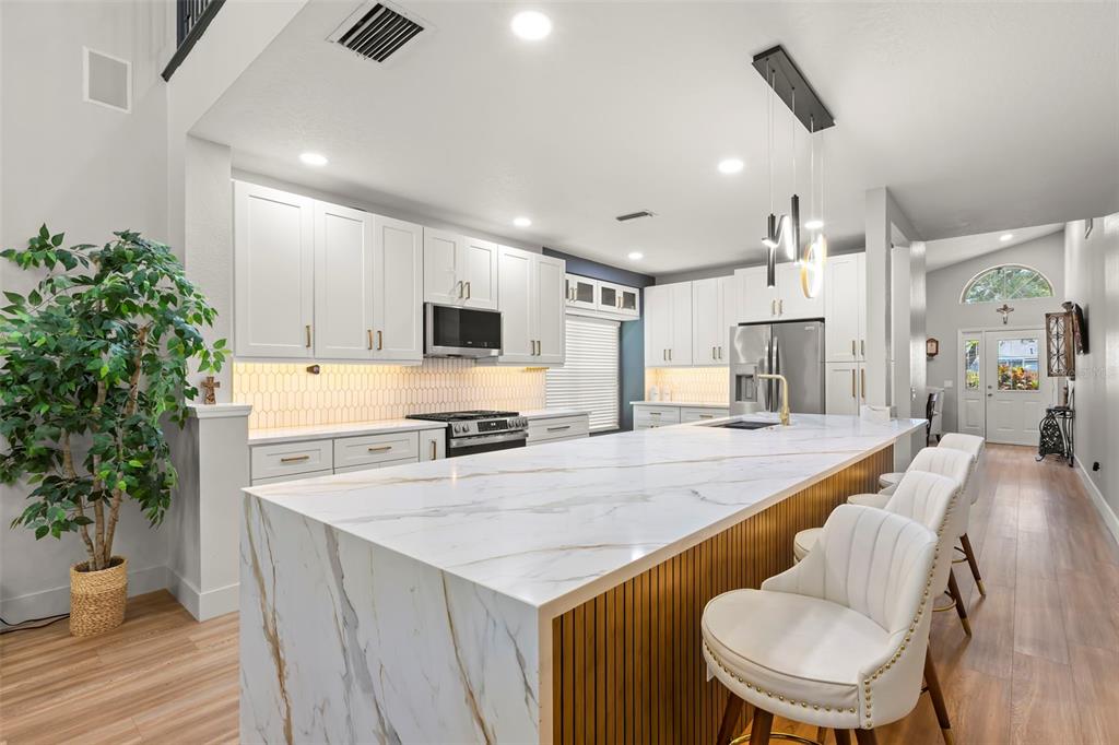A modern kitchen features white cabinetry, a large marble-topped island, and barstool seating — 9915 HARTWELL BRIDGE CIRCLE, TAMPA, FL