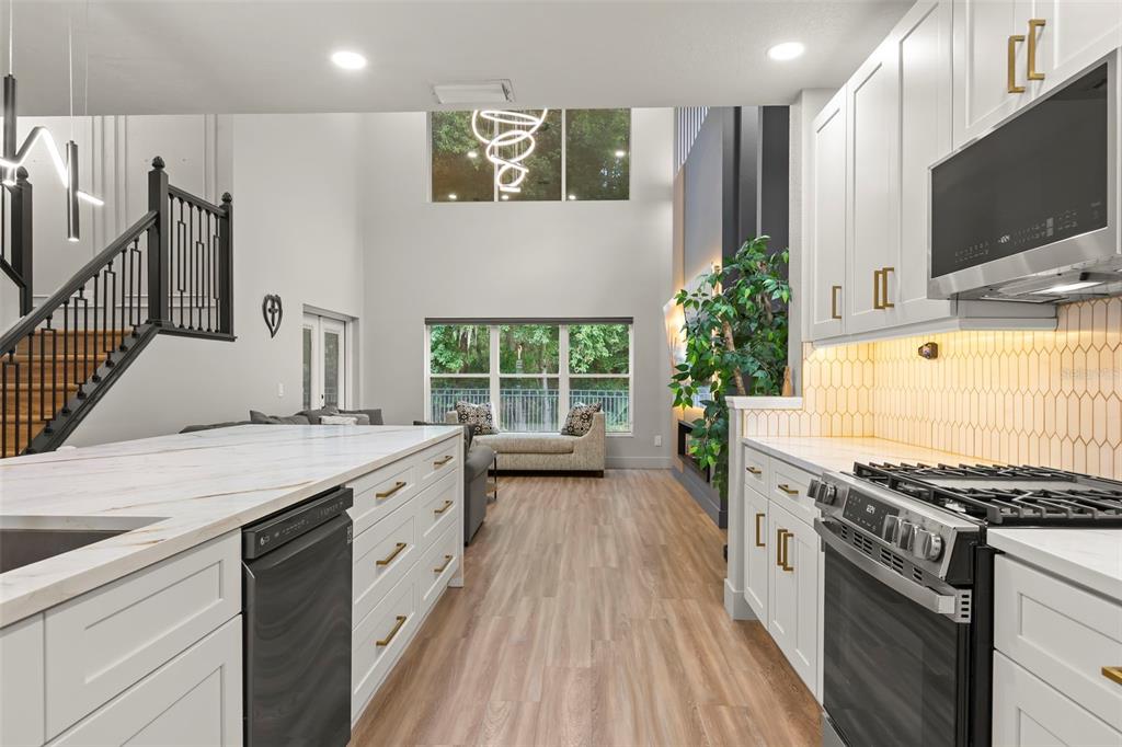 A modern kitchen with white cabinetry, marble countertops, and a large island overlooks a living area — 9915 HARTWELL BRIDGE CIRCLE, TAMPA, FL
