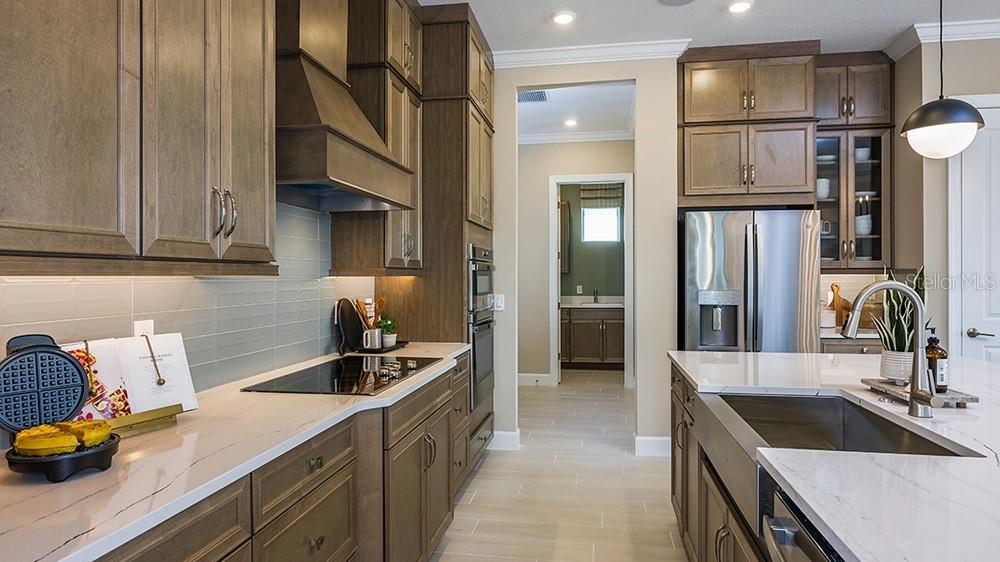A modern kitchen features wood cabinets, white countertops, stainless steel appliances, and a farmhouse sink — 7427 MOONBEAM AVENUE, SARASOTA, FL
