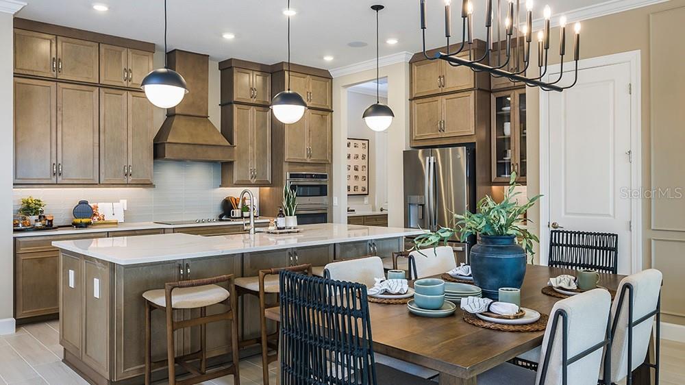 A modern kitchen features wood cabinets, a large island with bar seating, and a dining area — 7427 MOONBEAM AVENUE, SARASOTA, FL