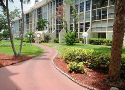 A paved walkway curves through a grassy lawn toward a multi-story apartment building — 851 Three Islands Blvd # 411, Hallandale Beach FL 33009, HALLANDALE BEACH, FL