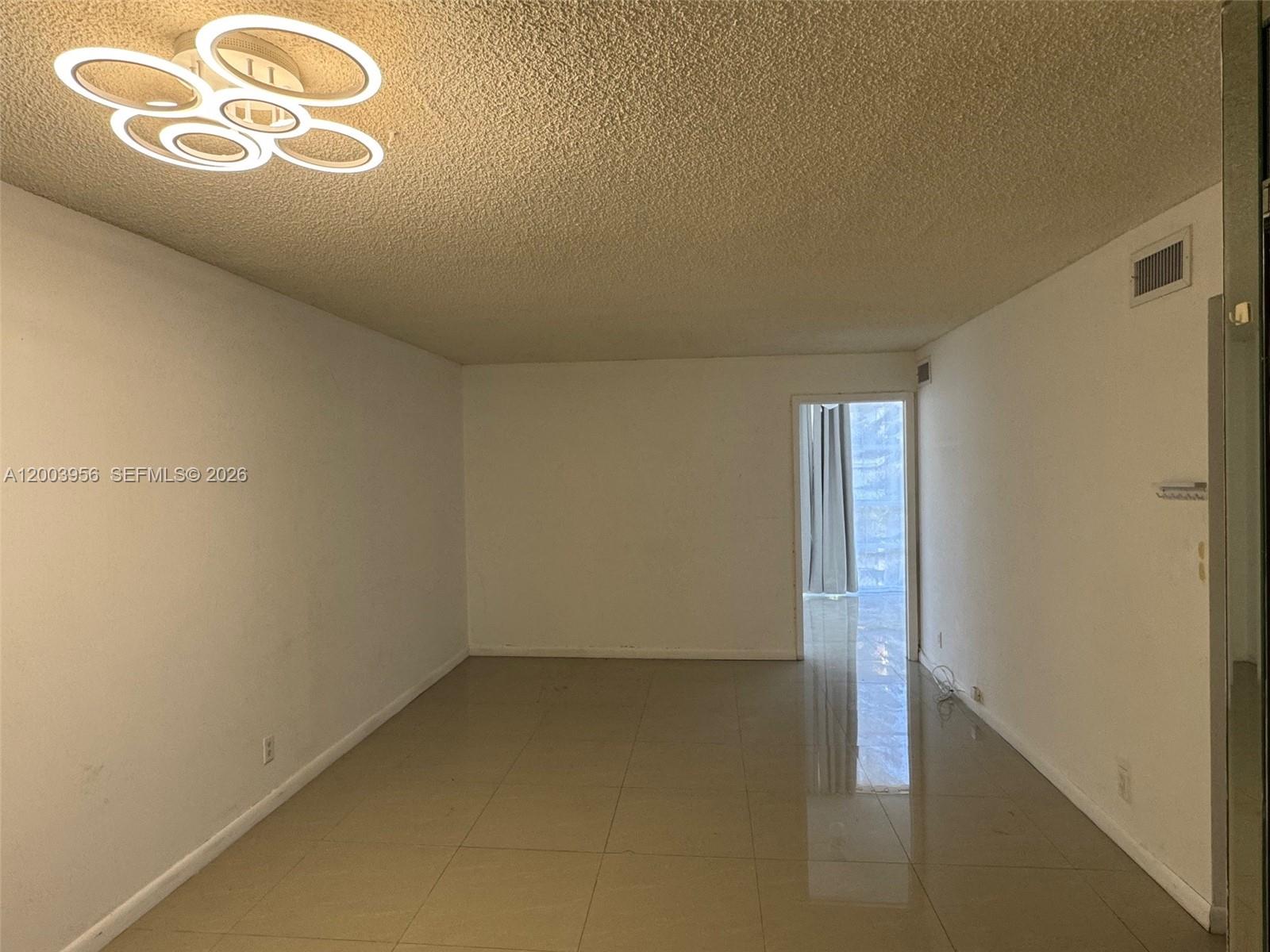 An empty room features white walls, a popcorn ceiling, tile flooring, and a modern light fixture — 851 Three Islands Blvd # 411, Hallandale Beach FL 33009, HALLANDALE BEACH, FL