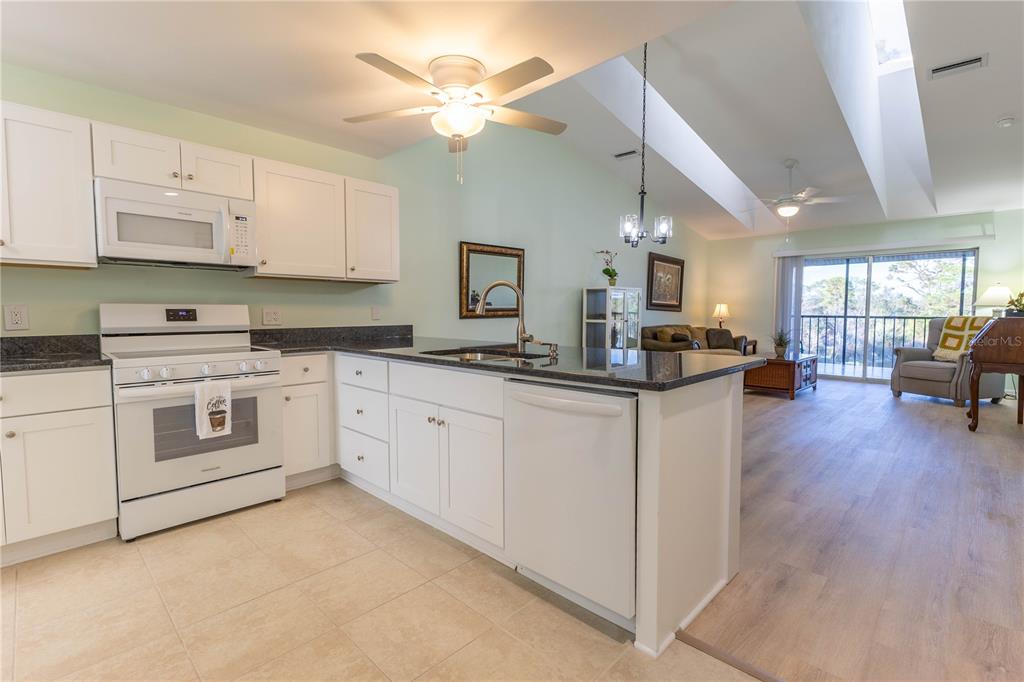 A kitchen with white cabinets and a breakfast bar opens into a living area — 6800 PLACIDA ROAD UNIT 268, ENGLEWOOD, FL