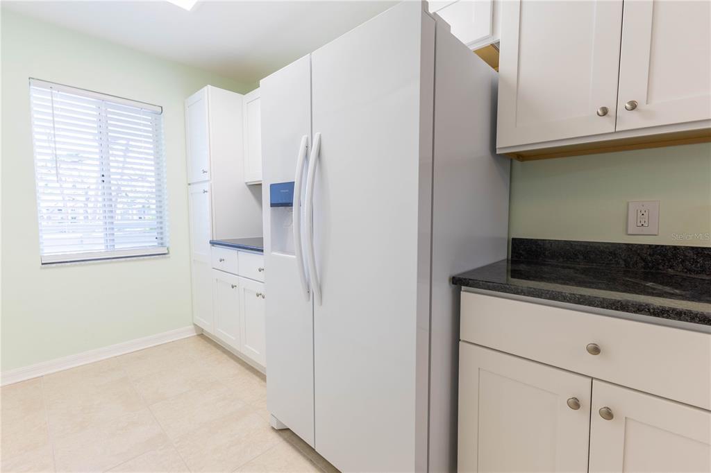 A kitchen features white cabinets, a side-by-side refrigerator, dark countertops, and a window with blinds — 6800 PLACIDA ROAD UNIT 268, ENGLEWOOD, FL
