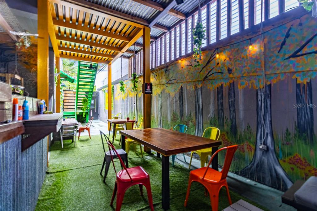 An outdoor patio features a wooden table, colorful chairs, artificial turf, and a mural wall — 1802 AVE FERNANDEZ JUNCOS, SAN JUAN, PR