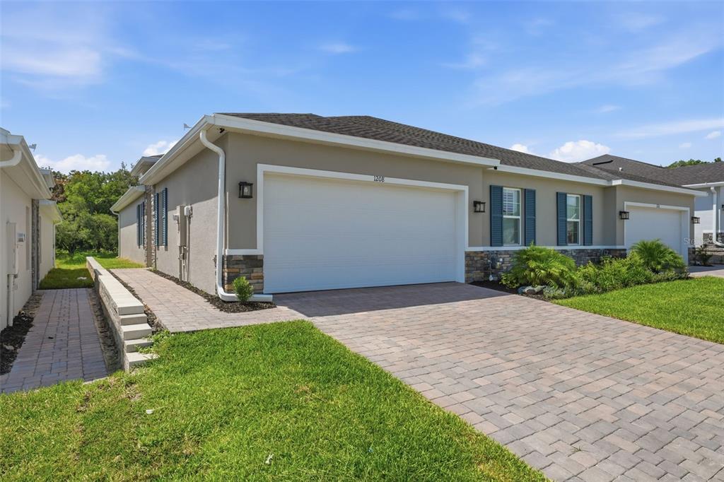 A beige house with a two-car garage, stone accents, and a paved driveway — 1208 TURTLE ISLAND ROAD, LADY LAKE, FL
