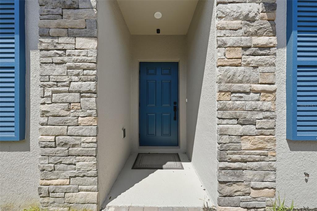 A blue front door is recessed between two stone-clad pillars with blue shutters on either side — 1208 TURTLE ISLAND ROAD, LADY LAKE, FL