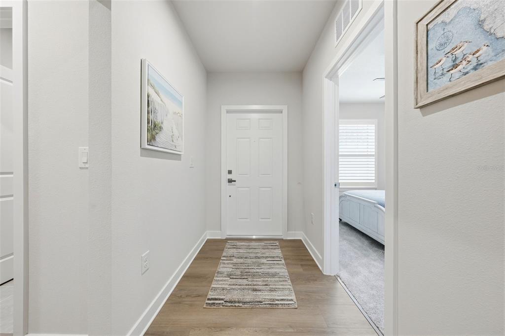 A bright entryway features light wood-look flooring, a white front door, and coastal wall art — 1208 TURTLE ISLAND ROAD, LADY LAKE, FL