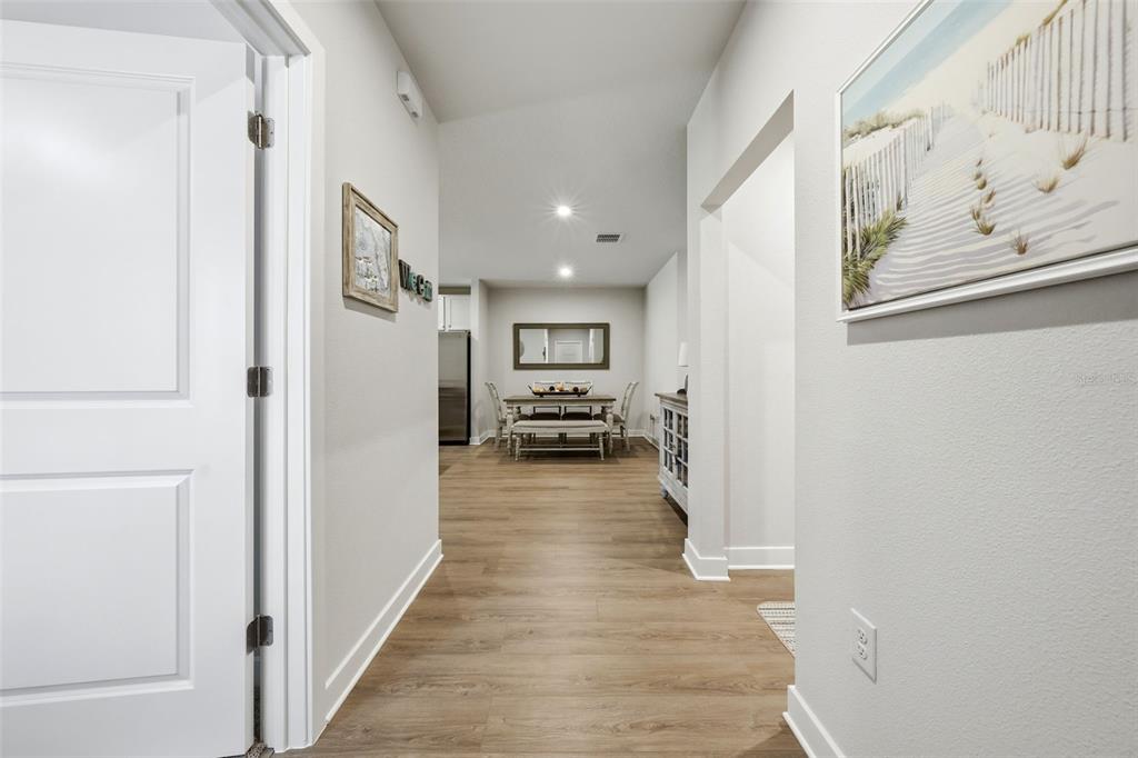 A hallway with light wood-look flooring leads to a dining area with a table — 1208 TURTLE ISLAND ROAD, LADY LAKE, FL