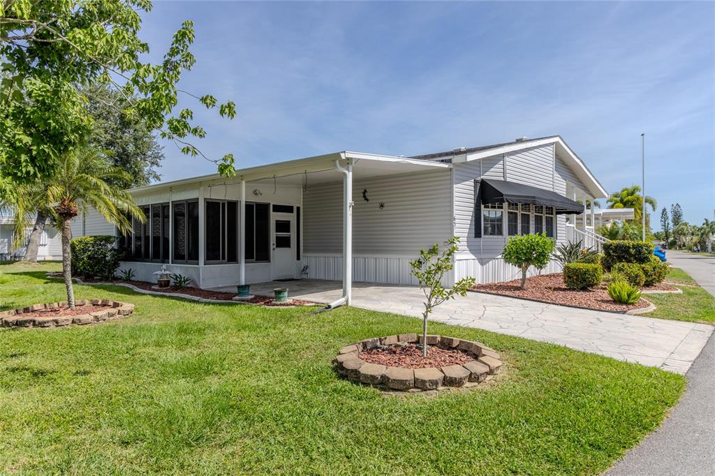 A single-story manufactured home with a screened porch, carport, and landscaped front yard — 2100 KINGS HIGHWAY UNIT 63, PORT CHARLOTTE, FL