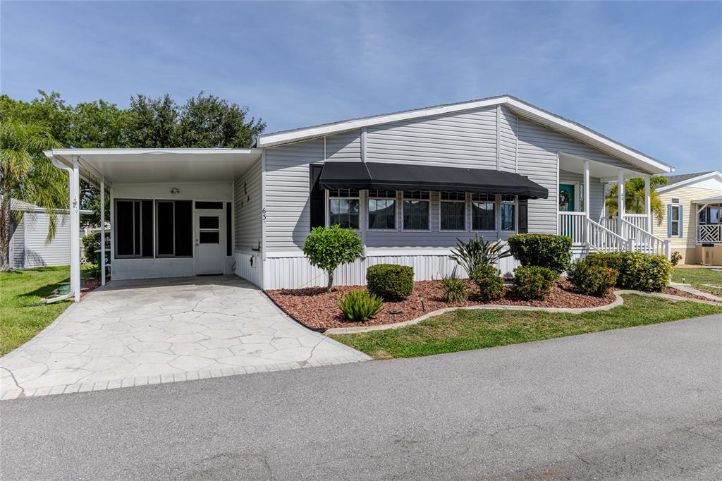A light gray manufactured home features a carport, a front porch, and landscaped garden beds — 2100 KINGS HIGHWAY UNIT 63, PORT CHARLOTTE, FL