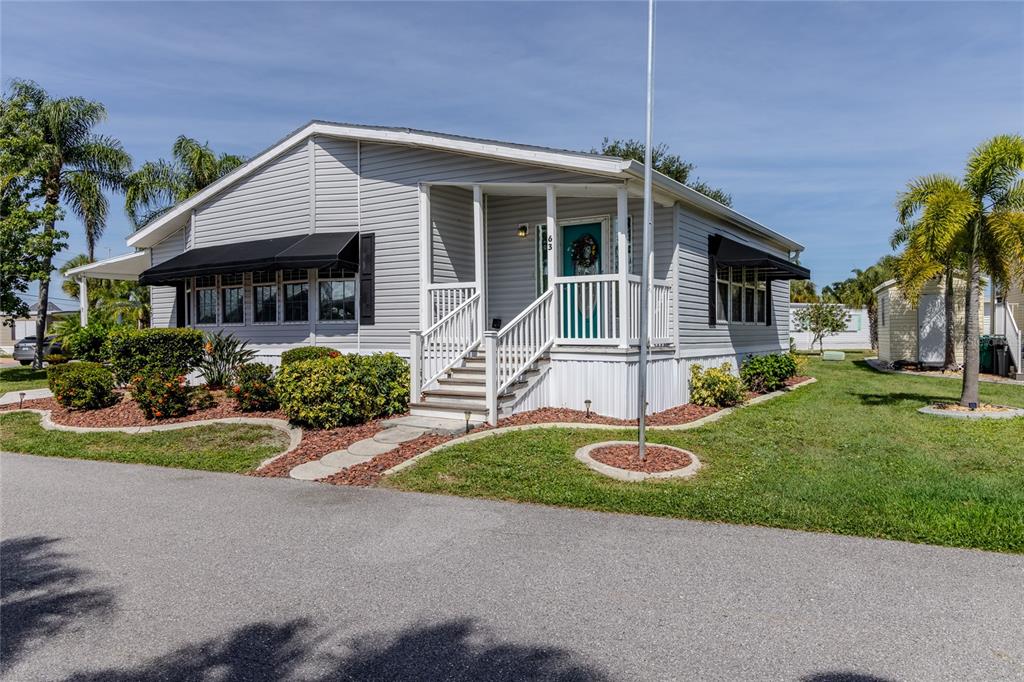 A light gray manufactured home features a front porch, black awnings, and a palm tree — 2100 KINGS HIGHWAY UNIT 63, PORT CHARLOTTE, FL