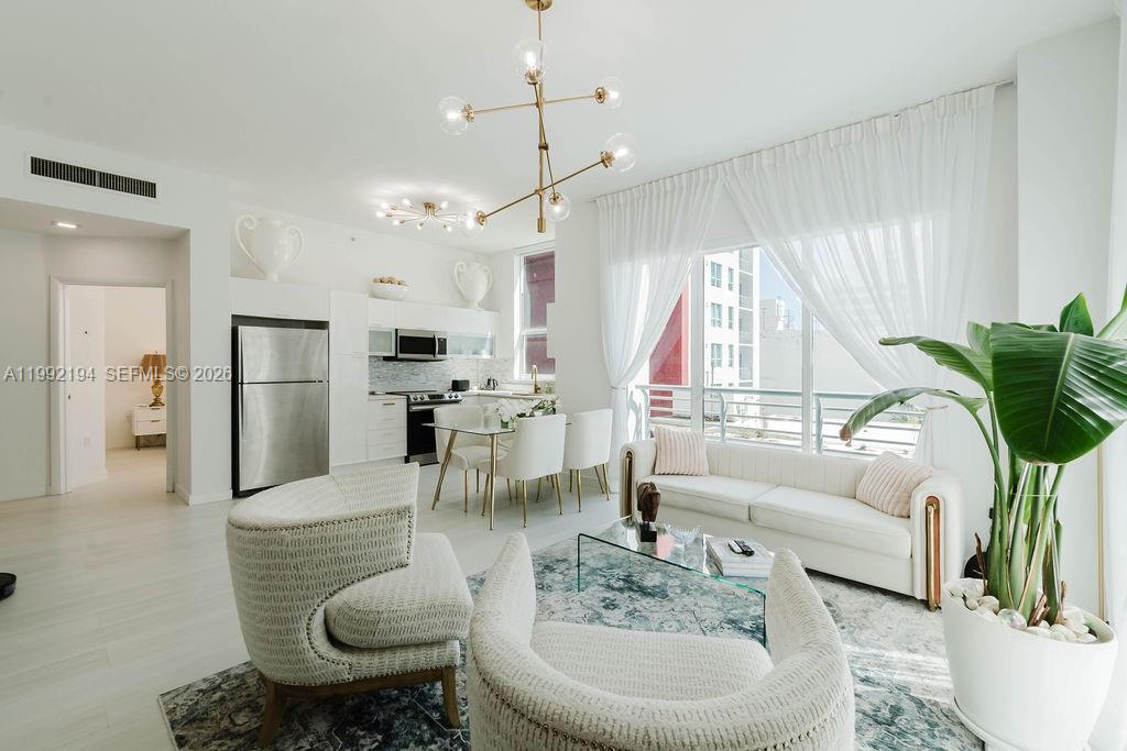 A bright, modern open-concept living and dining area features white furniture, a chandelier, and floor-to-ceiling windows — 133 NE 2nd Ave # 512, Miami FL 33132, MIAMI, FL