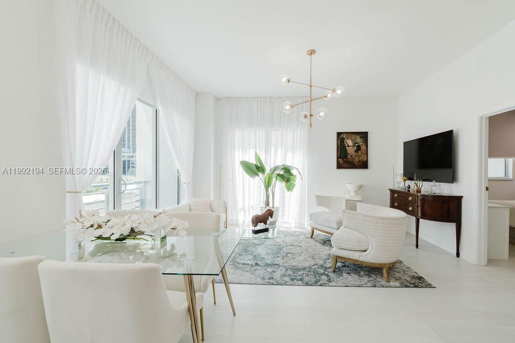 A bright, modern living and dining area features white furniture, a glass table, and sheer curtains — 133 NE 2nd Ave # 512, Miami FL 33132, MIAMI, FL