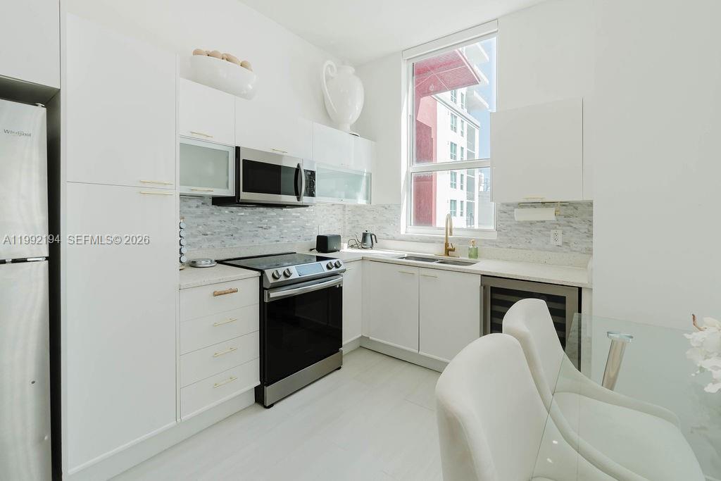 A modern white kitchen features stainless steel appliances, a tile backsplash, and a large window — 133 NE 2nd Ave # 512, Miami FL 33132, MIAMI, FL