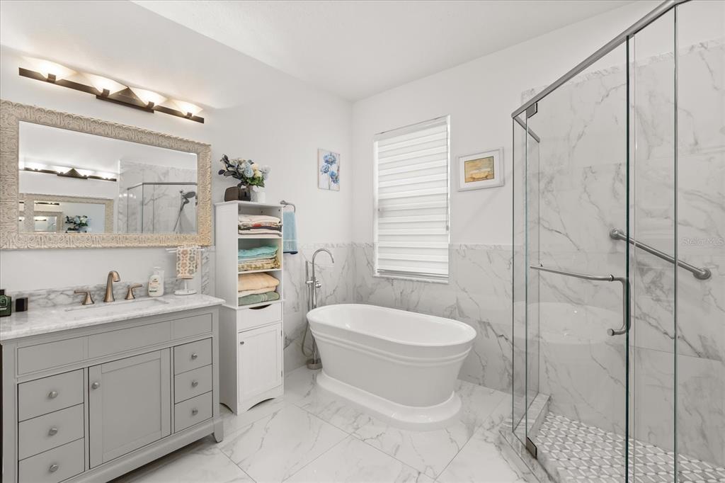 A bathroom features a gray vanity, a freestanding tub, and a glass-enclosed marble shower — 10180 CYPRESS VINE DRIVE, ORLANDO, FL
