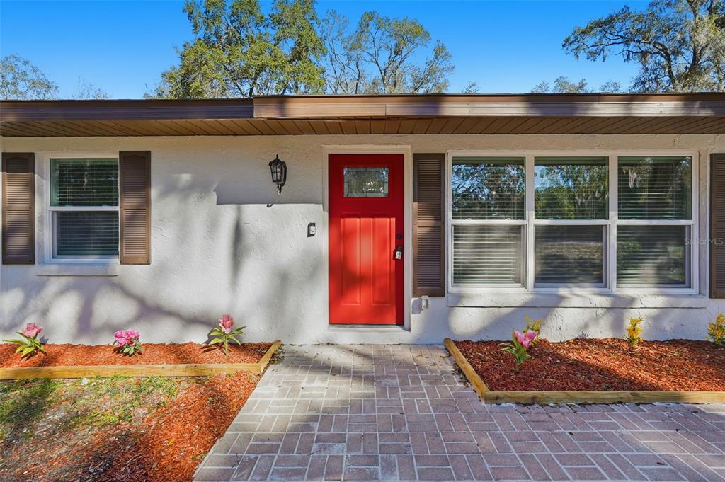 A red front door is centered on the exterior of a white house with shutters — 34071 MADISON AVENUE, DADE CITY, FL