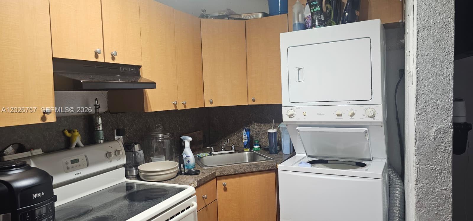 A kitchen features light wood cabinets, a stainless steel sink, and a stacked laundry unit — 3615 Thomas Ave # 13, Miami FL 33133, MIAMI, FL