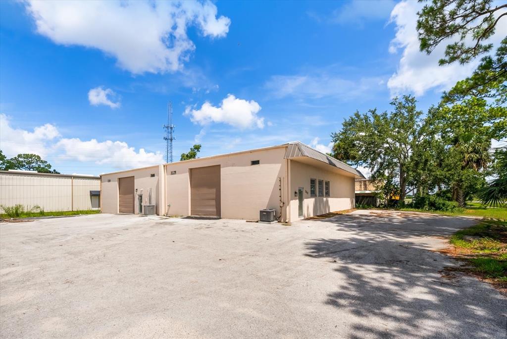 A tan, single-story commercial warehouse building with two roll-up doors and a paved parking lot — 260 POWER COURT UNIT 100-150, SANFORD, FL