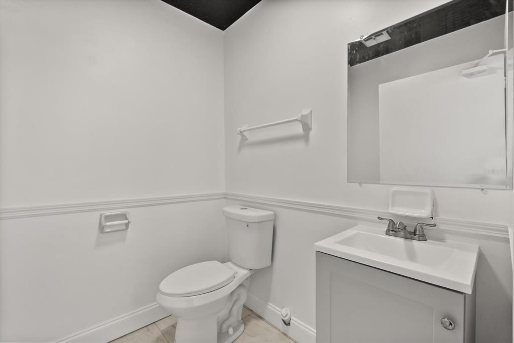 A bathroom features a white toilet, a grey vanity with a sink, and a wall mirror — 260 POWER COURT UNIT 100-150, SANFORD, FL