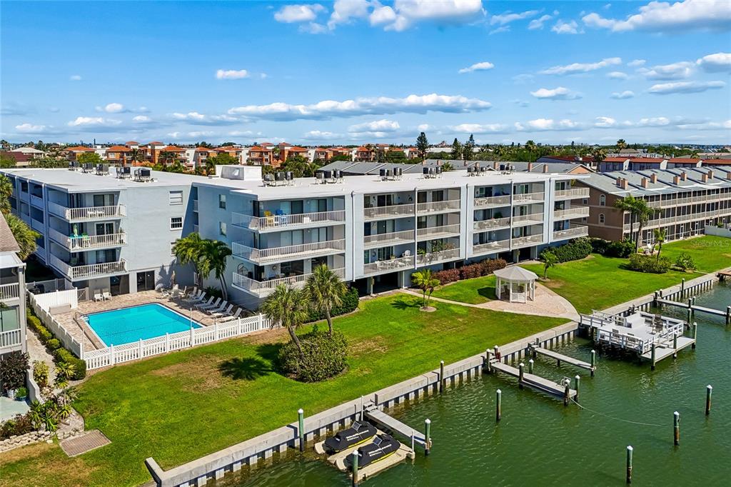 An aerial view shows a multi-story apartment complex with a swimming pool and boat docks — 719 PINELLAS BAYWAY S UNIT 301, ST PETERSBURG, FL