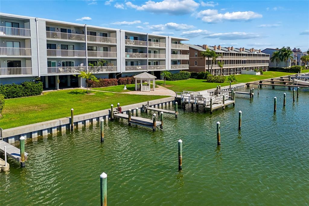An aerial view shows a multi-story apartment building with balconies overlooking a canal and docks — 719 PINELLAS BAYWAY S UNIT 301, ST PETERSBURG, FL