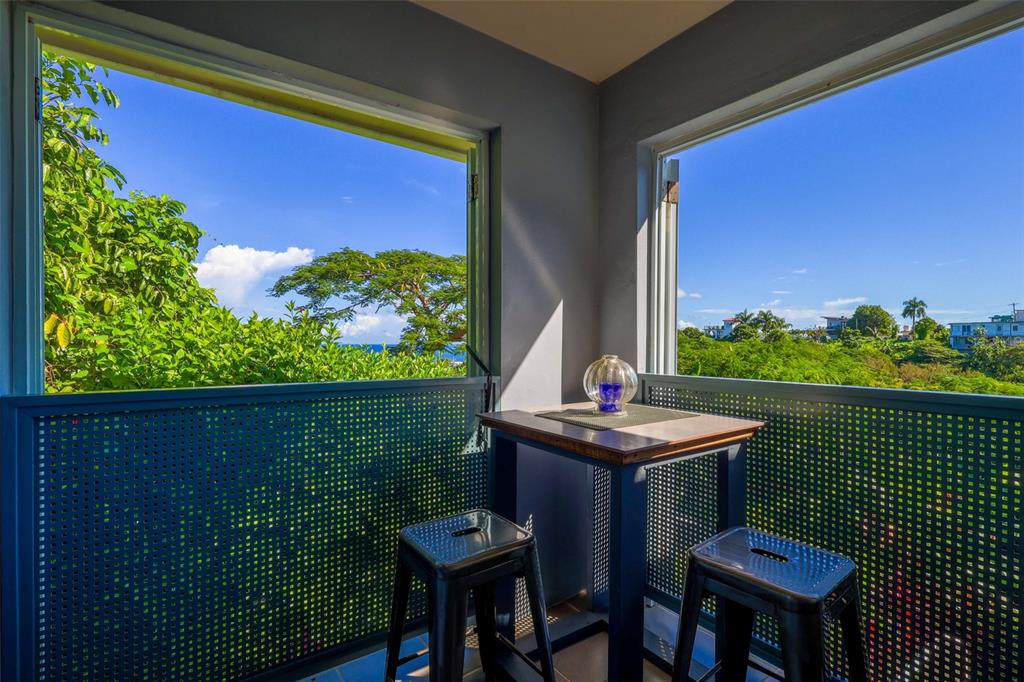 A balcony with a small table, two stools, and views of trees and the ocean — Km 4.4 CARR 413 PUNTAS, RINCON, PR