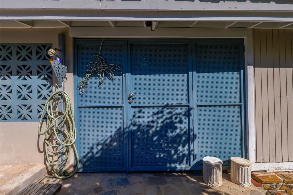A blue metal screen door is mounted on a patio with a garden hose — Km 4.4 CARR 413 PUNTAS, RINCON, PR
