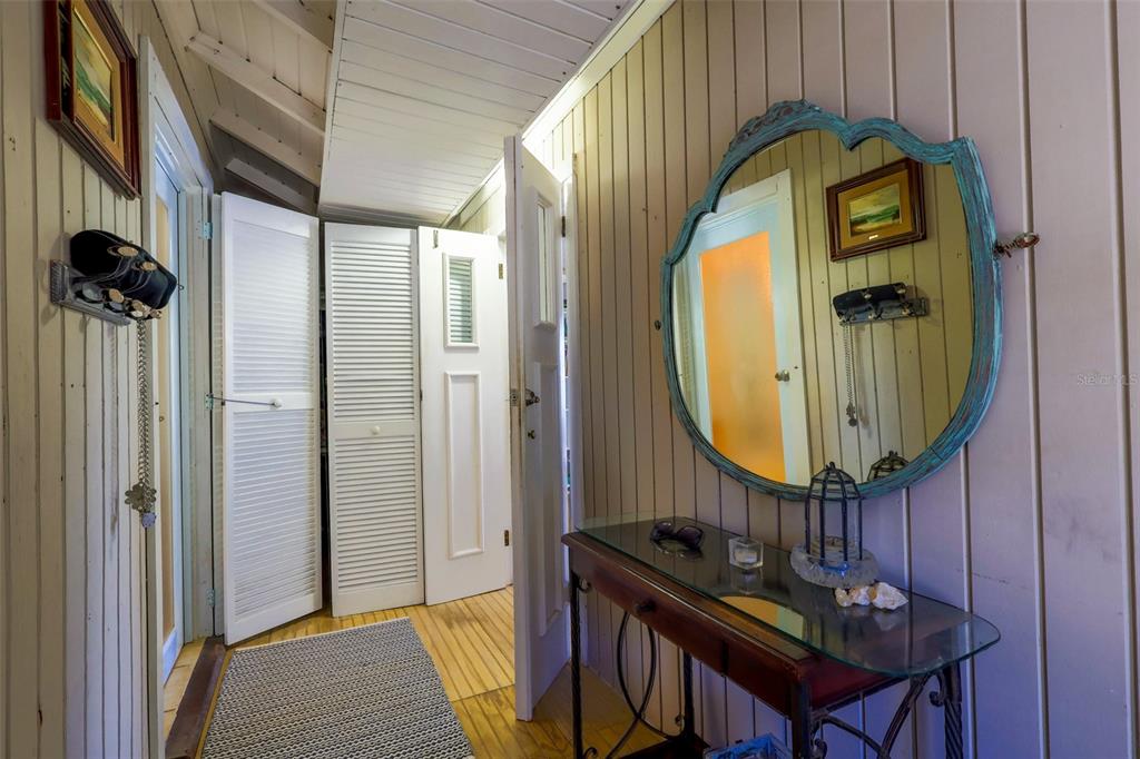 A hallway with wood-paneled walls, a glass-topped console table, a decorative mirror, and louvered doors — Km 4.4 CARR 413 PUNTAS, RINCON, PR