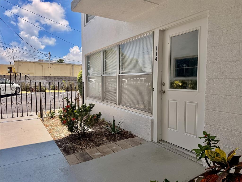 A white building exterior features a front door numbered 114, large windows, and landscaping — 3100 HARTFORD STREET N UNIT 114, ST PETERSBURG, FL